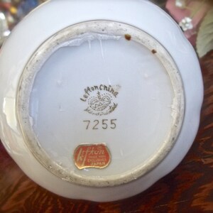 Peut inclure: Vase en porcelaine blanche avec un bord dor&eacute; et un motif floral. Le fond de la vase porte une &eacute;tiquette dor&eacute;e avec le texte "Le Mon China Hand Painted" et le num&eacute;ro "7255". Il y a &eacute;galement une &eacute;tiquette rouge avec le texte "Kiffin Made in Japan Exclusive".