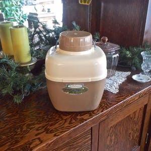 May include: A brown and white insulated beverage dispenser with a handle. The dispenser has a label that reads "Ballantine's Light Insulated Jug".