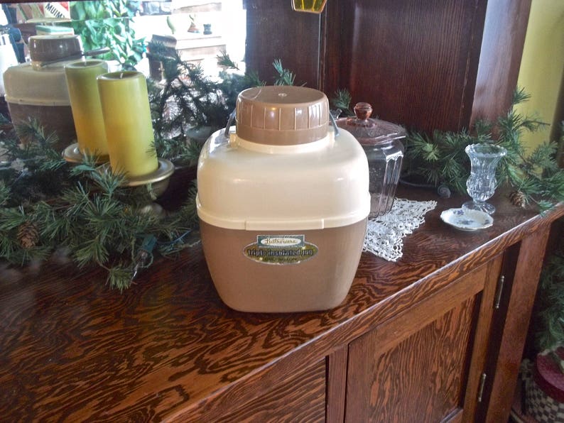 May include: A brown and white insulated beverage dispenser with a handle. The dispenser has a label that reads "Ballantine's Light Insulated Jug".