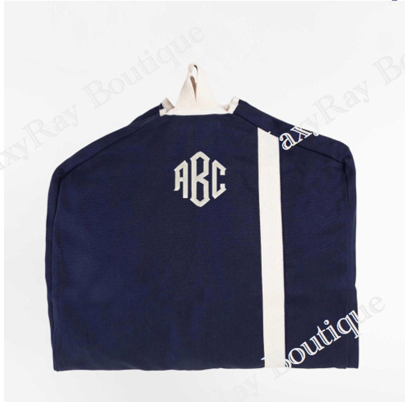 May include: A navy blue garment bag with a white stripe down the side. The bag has a white monogram "ABC" embroidered on the front.