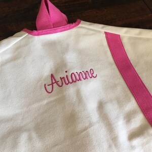 May include: White garment bag with a pink trim and a pink stripe down the side. The bag is personalized with the name "Arianne" embroidered in pink.
