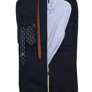 May include: A navy blue garment bag with a white zipper and a brown leather belt. The bag has a pocket on the front with a tie and a pocket on the back with a shirt.