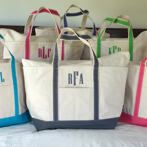 Op de afbeelding: Een collectie off-white canvas draagtassen met gekleurde randen en hengsels. Elke tas is voorzien van een monogram van drie letters, geborduurd in een bijpassende kleur garen, met accenten in turquoise, felroze, marineblauw, limoengroen en donkergrijs.