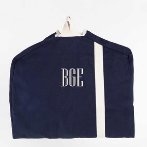 May include: A navy blue garment bag with a white stripe down the side and the monogram "BGE" embroidered on the front.