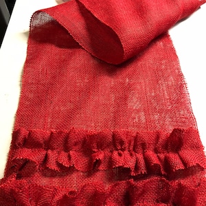 May include: Red burlap table runner with a double row of ruffles along the bottom edge.