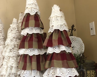 May include: Two tiered Christmas trees made of fabric. The trees are decorated with white lace and red and green plaid fabric. The larger tree has a wooden star on top.