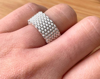 May include: A silver ring with a woven design. The ring is on a person's finger.