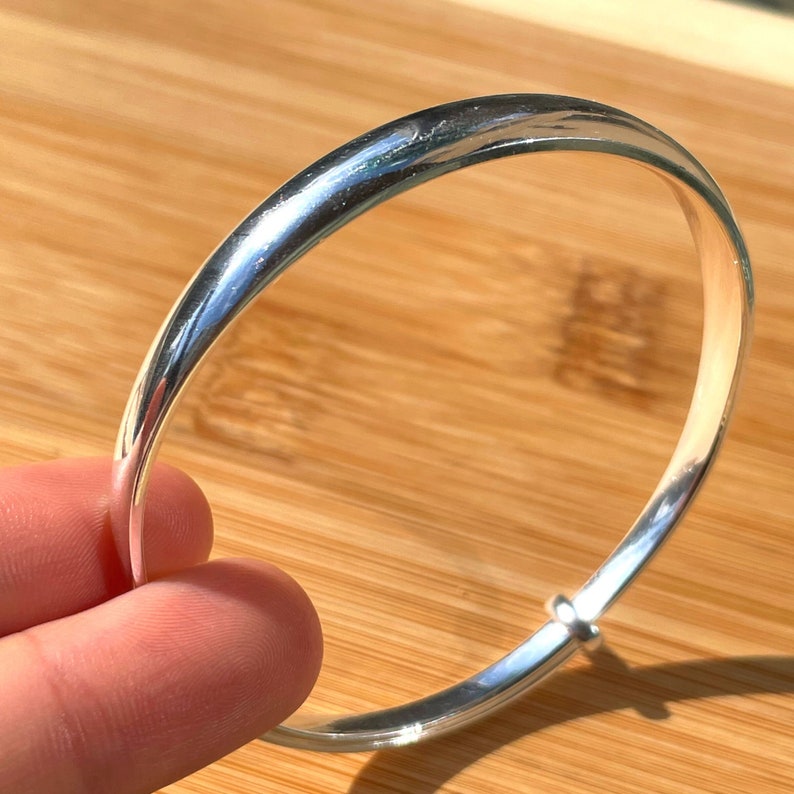 May include: A silver bangle bracelet with a smooth, polished finish. The bracelet has a hinged clasp.