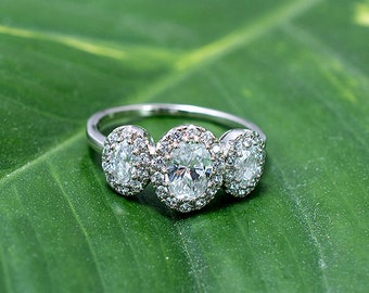May include: A silver ring with three oval-shaped diamonds set in a halo setting. The diamonds are surrounded by smaller diamonds.