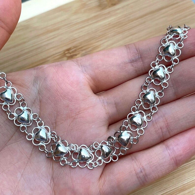 May include: A silver necklace with a double row of heart-shaped charms connected by delicate chain links.