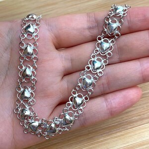 May include: A silver chain necklace with a delicate heart design. The chain is made of small, interconnected hearts, creating a continuous pattern.