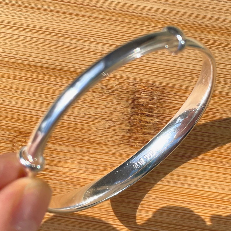 May include: A silver bangle bracelet with a simple design. The bracelet has a smooth, polished finish and a small, round clasp.