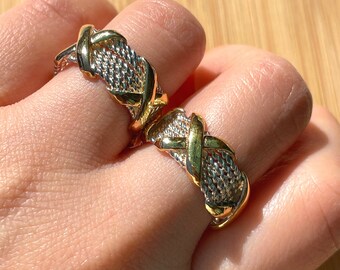 May include: Two gold and silver rings with a braided design. The rings are worn on the fingers of a person's hand.