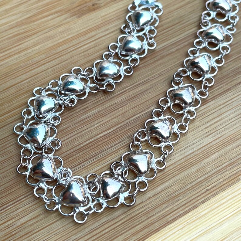 May include: A silver necklace with a delicate chain and heart-shaped links. The necklace is made of multiple strands of chain, each with a series of small, heart-shaped charms.