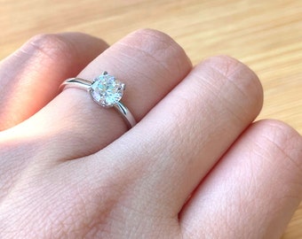 May include: A silver ring with a clear round gemstone.