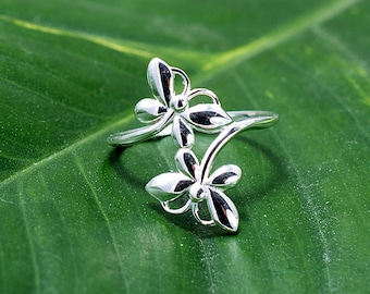 May include: A silver ring with a delicate design of two stylized flowers connected by a stem. The ring is set against a green leaf background.