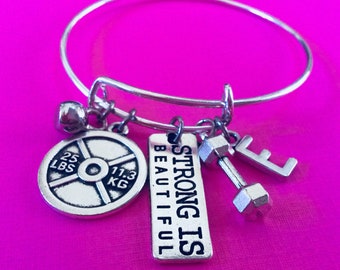 May include: Silver charm bracelet with a dumbbell, weight plate, bell, and a charm that says "Strong is Beautiful".