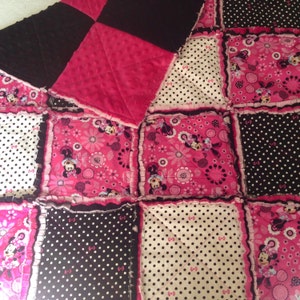 Pode incluir: Uma colcha de retalhos rosa e preta com tema do Mickey Mouse. A colcha &eacute; feita de v&aacute;rios tecidos, incluindo bolinhas, estampas florais e cores s&oacute;lidas. A colcha &eacute; guarnecida com uma bainha de babados.