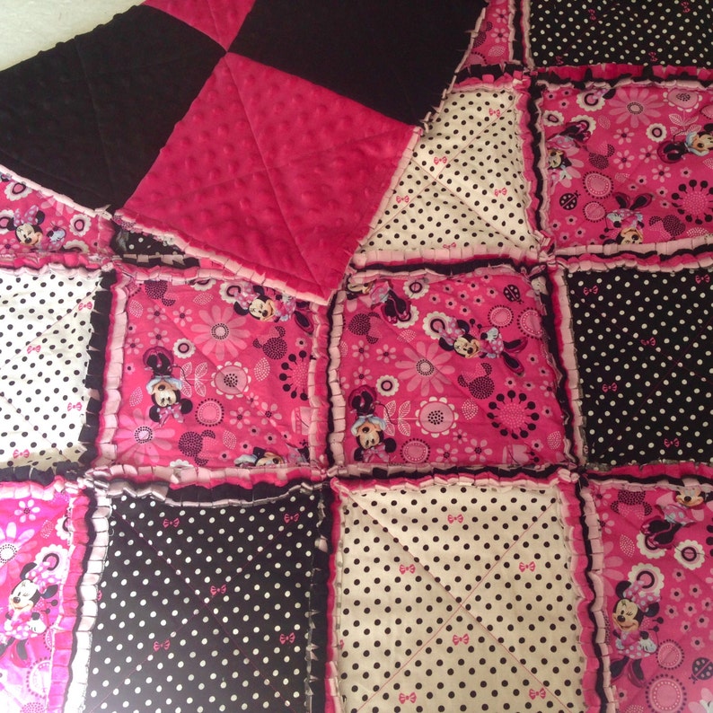 Pode incluir: Uma colcha de retalhos rosa e preta com tema do Mickey Mouse. A colcha &eacute; feita de v&aacute;rios tecidos, incluindo bolinhas, estampas florais e cores s&oacute;lidas. A colcha &eacute; guarnecida com uma bainha de babados.