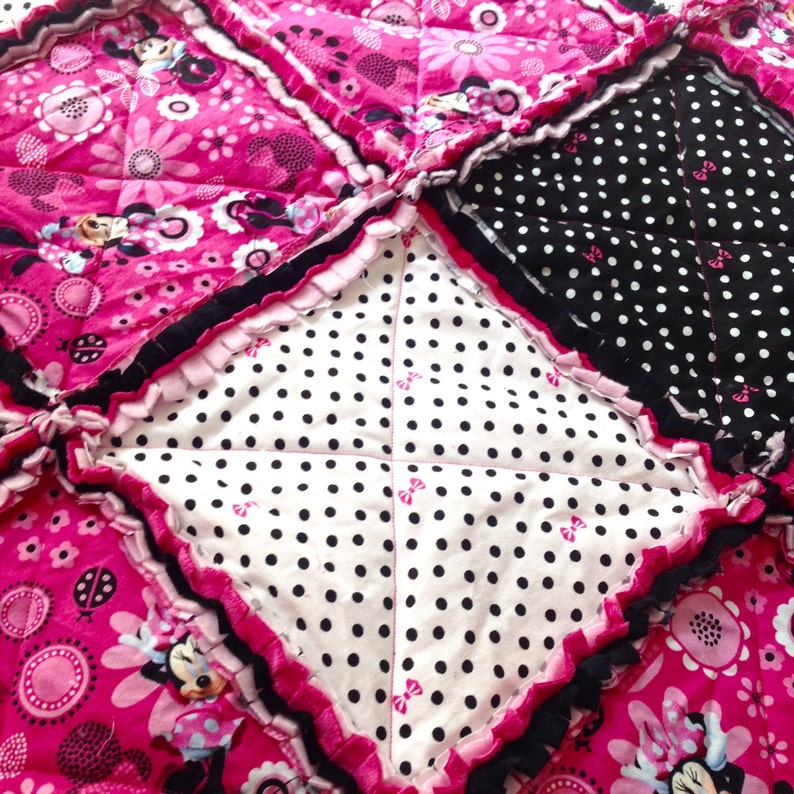 Pode incluir: Uma colcha de retalhos rosa e preta com um centro branco com bolinhas pretas. A colcha &eacute; feita com uma variedade de tecidos, incluindo um tecido rosa com padr&atilde;o floral e um tecido preto com bolinhas brancas. A colcha &eacute; guarnecida com um babado rosa.