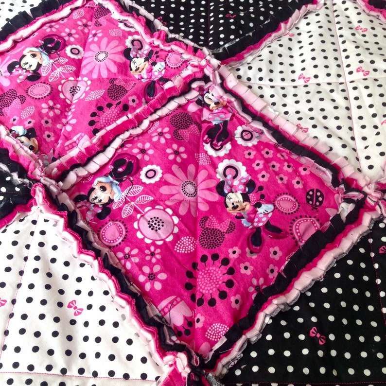 Pode incluir: Uma colcha de retalhos rosa e preta com estampa de Minnie Mouse. A colcha &eacute; feita de quadrados de tecido com diferentes padr&otilde;es, incluindo bolinhas, flores e personagens da Minnie Mouse.