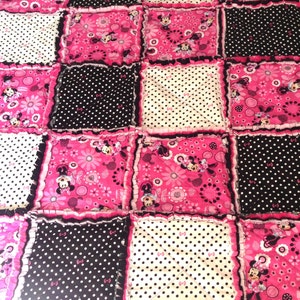 Pode incluir: Uma colcha de retalhos rosa e preta com tema Minnie Mouse. A colcha &eacute; feita de v&aacute;rios tecidos com bolinhas, flores e imagens da Minnie Mouse.