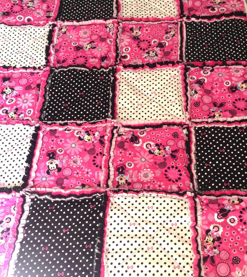 Pode incluir: Uma colcha de retalhos rosa e preta com tema Minnie Mouse. A colcha &eacute; feita de v&aacute;rios tecidos com bolinhas, flores e imagens da Minnie Mouse.