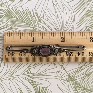 Op de afbeelding: Een zilveren broche met een paarse edelsteen in een bloemmotief. De broche is ongeveer 3,8 cm lang.