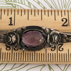 Op de afbeelding: Een zilveren ring met een paarse edelsteen gezet in een bloemmotief. De ring heeft een diameter van ongeveer 2,5 cm.