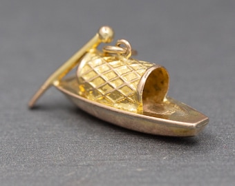 May include: A gold-colored charm in the shape of a gondola with a small oar. The gondola has a checkered pattern on the top and a small loop for attaching it to a chain.