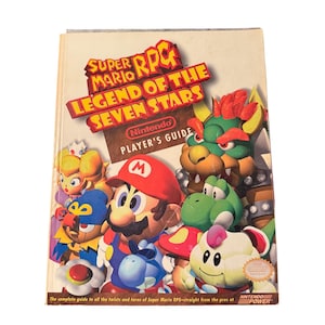 May include: A vintage Super Mario RPG: Legend of the Seven Stars Nintendo Player's Guide. The cover features colorful illustrations of Mario, Princess Peach, Bowser, and other characters. The guide includes the Nintendo Power logo.