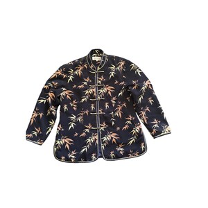 Puede incluir: Una chaqueta de manga larga en azul marino oscuro con cuello mao y un patrón repetitivo de hojas de bambú en tonos naranja, amarillo y blanco. La chaqueta incluye cinco cierres de palanca cubiertos de tela en el centro frontal.