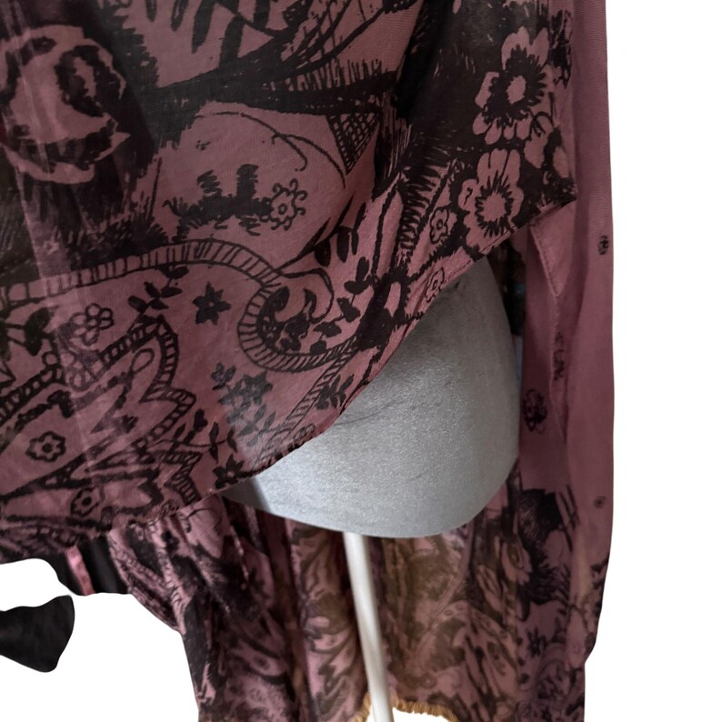 Puede incluir: Un vestido largo, transparente, de color rosa y negro con un dise&ntilde;o floral. El vestido tiene un cuello alto y mangas largas. La tela es ligera y fluida.
