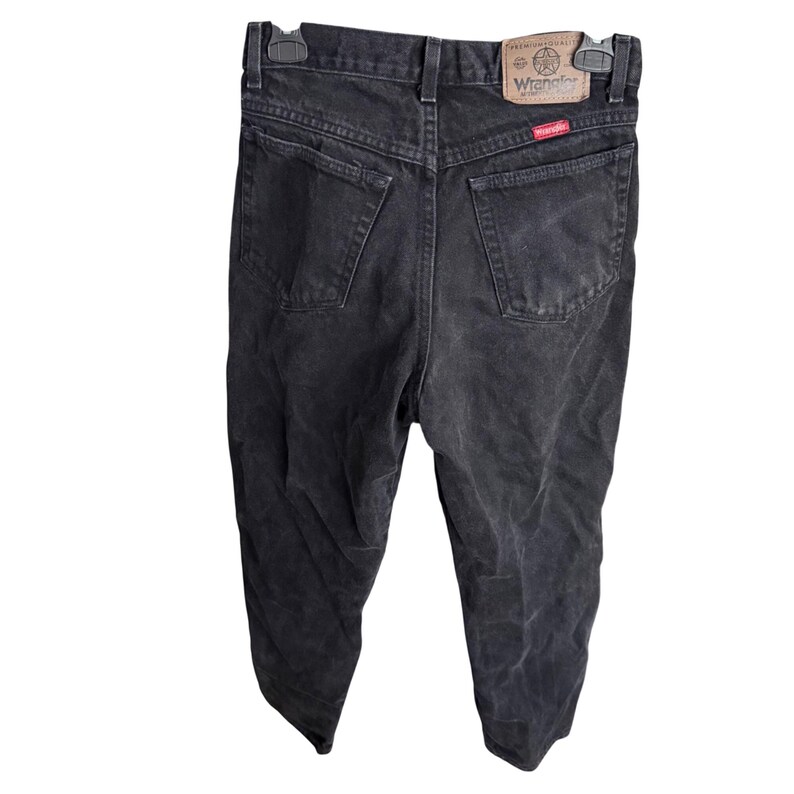 May include: Black Wrangler jeans with a faded appearance. The jeans have a classic five-pocket design, a button and zipper closure, and a leather patch with the Wrangler logo on the back. The jeans are hanging on a black hanger.