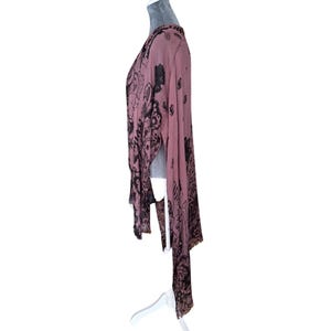 Puede incluir: Una blusa de manga larga, rosa y transparente con estampado floral negro. La blusa tiene cuello en V y un dobladillo asim&eacute;trico fluido.