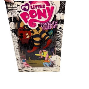Puede incluir: Una portada de cómic de "My Little Pony Treasury Edition" con ponis de dibujos animados y una criatura con forma de araña. La portada tiene un fondo blanco con telarañas en blanco y negro y otras ilustraciones.