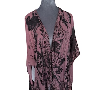 Puede incluir: Un kimono largo y fluido de color malva con un estampado paisley negro. El kimono tiene un cuello en V profundo y mangas largas.