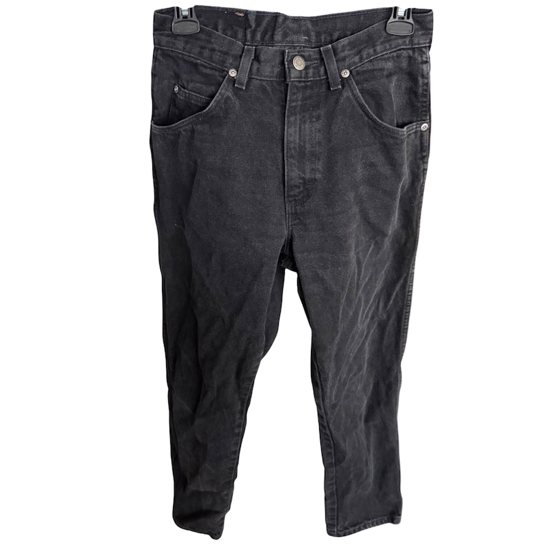 May include: Black denim jeans with a classic five-pocket design. The jeans have a button and zipper closure, belt loops, and a straight leg fit. The fabric appears slightly faded, giving them a worn-in look.