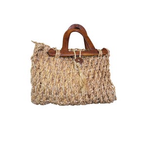 May include: A handbag crafted from thick, light brown woven rope featuring two dark brown polished wooden handles. The bag includes a central wooden button closure with a dangling rope tassel detail, showcasing a textured, open-weave design.