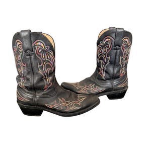 Könnte beinhalten: Ein Paar schwarze Leder-Cowboystiefel mit farbenfroher Blumenstickerei. Die Stiefel haben eine spitze Zehenpartie und einen gestapelten Absatz. Die Stickerei weist Farbtöne von Rot, Gelb, Rosa und Blau auf.