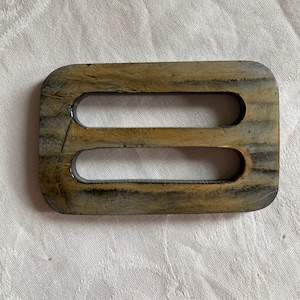May include: A wooden belt buckle with two oval-shaped cutouts. The buckle is a dark brown color with a light brown wood grain pattern.