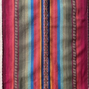 K&ouml;nnte beinhalten: Ein farbenfrohes gewebtes Textil mit vertikalen Streifen in Rot, Blau, Orange und Gr&uuml;n. Ein zentrales Rautenmuster und dekorative Bord&uuml;ren erg&auml;nzen das Design. Das Textil ist wahrscheinlich ein Teppich oder eine Decke, etwa 150 cm lang.