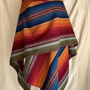 Könnte beinhalten: Ein farbenfroher gestreifter Poncho mit geometrischem Muster. Der Poncho ist aus gewebtem Stoff gefertigt und hat eine Vielzahl von Farben, darunter Rot, Orange, Gelb, Blau und Grün.