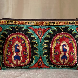 Könnte beinhalten: Eine tealblaue Stofftasche mit Reißverschluss. Die Tasche hat ein farbenfrohes Stickmuster mit roten, gelben, schwarzen und blauen Akzenten. Das Muster erinnert an traditionelle türkische oder orientalische Muster.