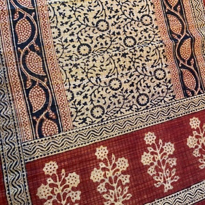 May include: A red fabric with a black and white floral pattern. The fabric has a border with a repeating pattern of black and white waves. The fabric has a repeating pattern of small, white flowers on a red background.