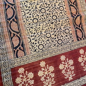 May include: A red fabric with a black and white floral pattern. The fabric has a border with a repeating pattern of black and white waves. The fabric has a repeating pattern of small, white flowers on a red background.