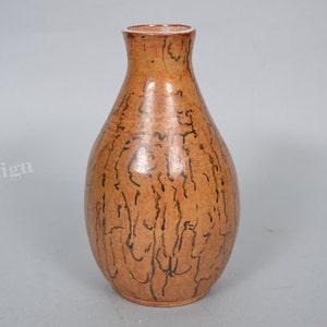 May include: A brown ceramic vase with a narrow neck and a rounded body. The vase has a black and brown abstract design.