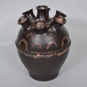 May include: A dark brown ceramic vase with six openings on the top. The vase has a decorative design around the middle.