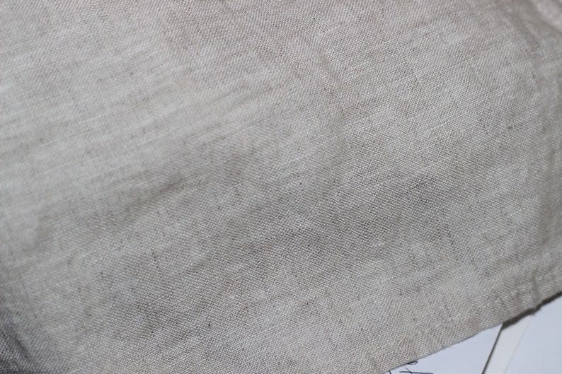 Puede incluir: Una vista de cerca de una tela de color beige claro natural con una textura tejida visible. El material presenta un patr&oacute;n de trama cruzada distintivo caracter&iacute;stico del lino, mostrando variaciones sutiles en el color del hilo y un tejido irregular.
