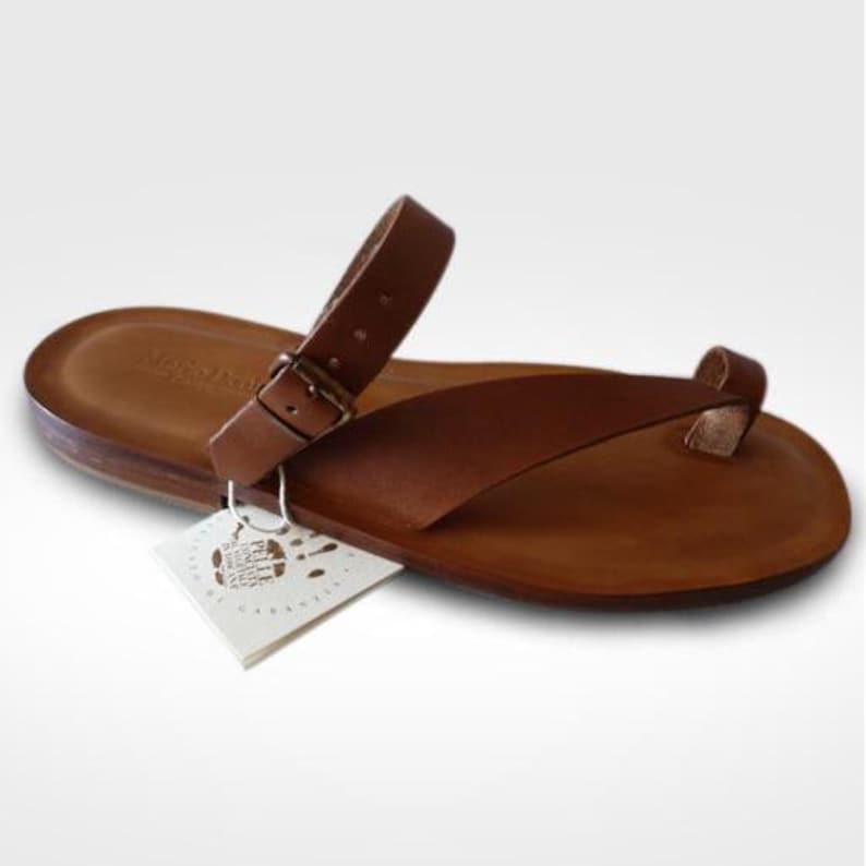 May include: Brown leather thong sandals with a buckle closure. The sandals have a simple design and are made of high-quality leather.